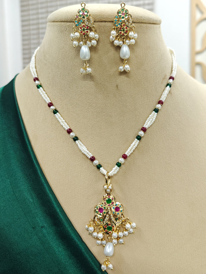 Close-up of an ornate traditional (Gold Polish) Multi-Color Pendant Set and Earrings with  Pearl and Colored Stones. Festive saree look completed with a handcrafted Jadau Pendant. Close-up of high-quality Jadau artificial Pendant craftsmanship.