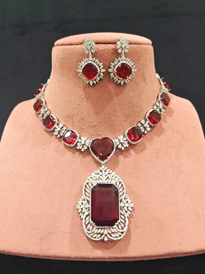 Close-up of an ornate Western (Silver Polish) Red Collar Jewellery Set and Earrings with American Diamond and Red Colored Stones. Party wear outfit completed with a lightweight Colored Stone necklace. Close-up of a cocktail party look featuring a premium Colored Stone necklace.