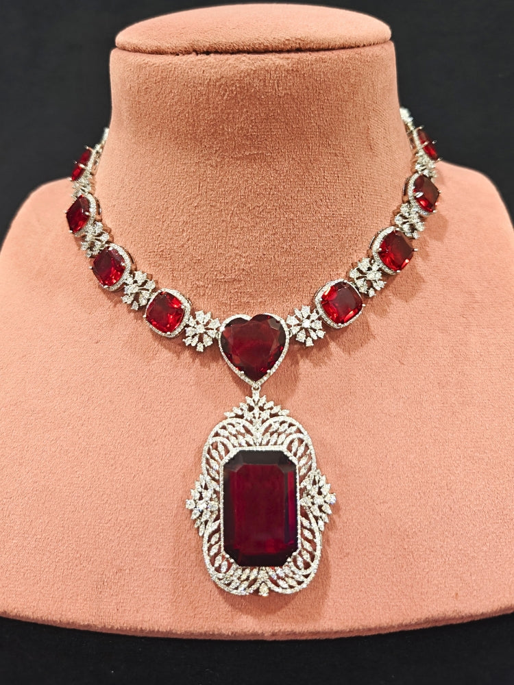 Close-up of an ornate Western (Silver Polish) Red Collar Jewellery Set and Earrings with American Diamond and Red Colored Stones. Party wear outfit completed with a lightweight Colored Stone necklace. Close-up of a cocktail party look featuring a premium Colored Stone necklace.