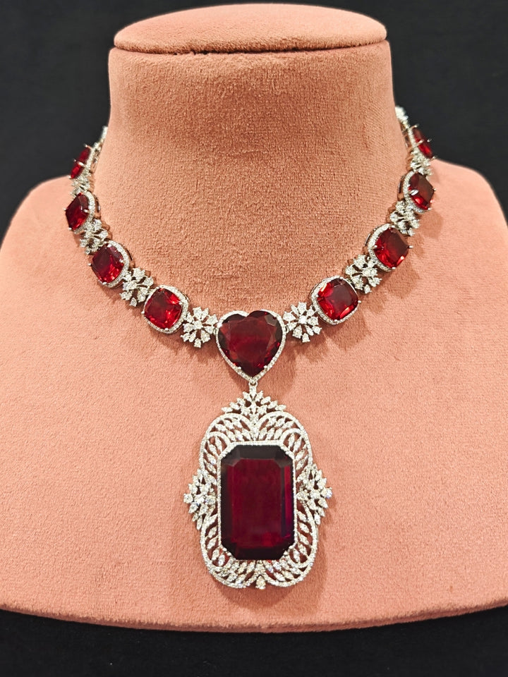 Close-up of an ornate Western (Silver Polish) Red Collar Jewellery Set and Earrings with American Diamond and Red Colored Stones. Party wear outfit completed with a lightweight Colored Stone necklace. Close-up of a cocktail party look featuring a premium Colored Stone necklace.