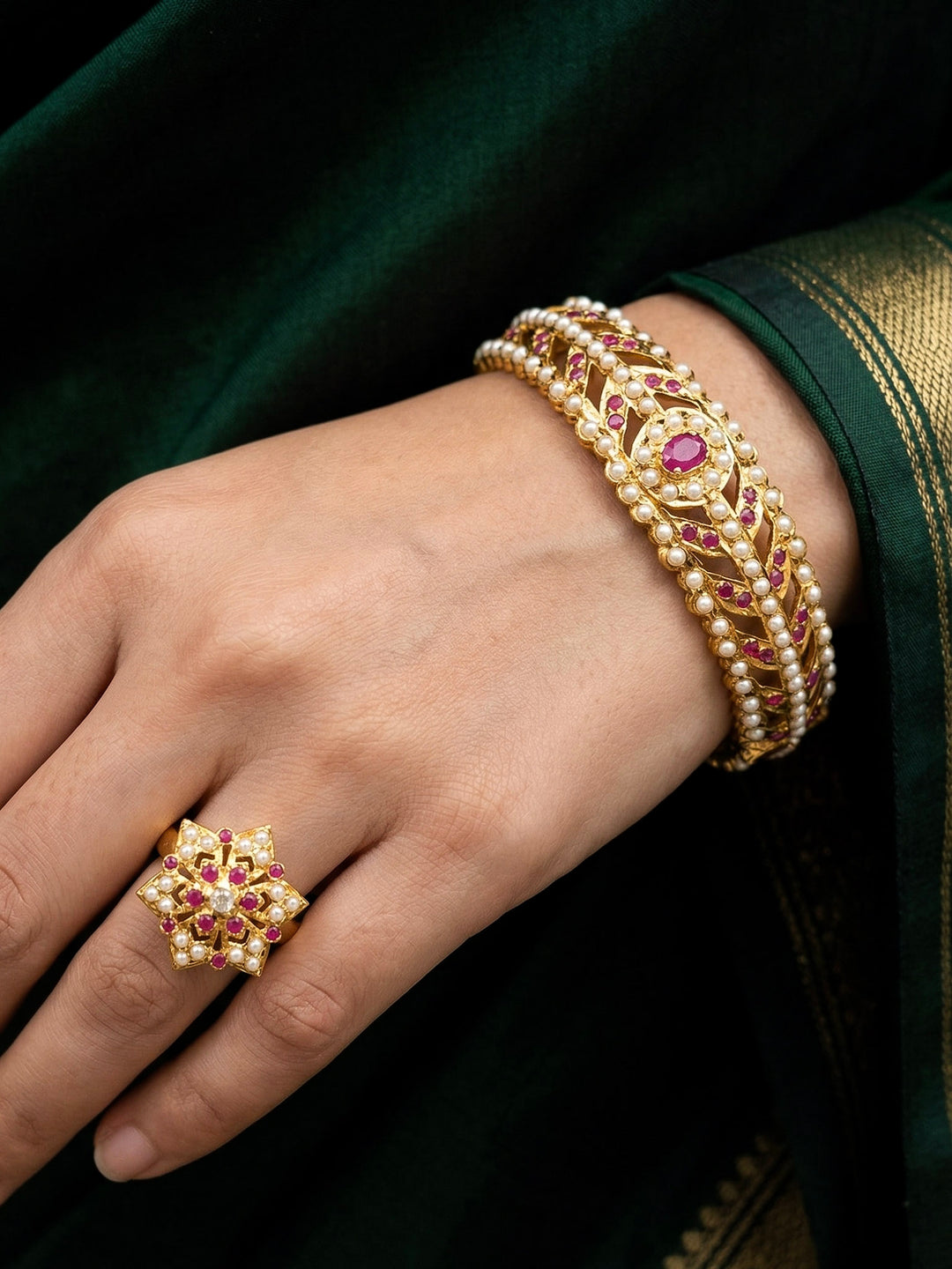 Close-up of a woman wearing an ornate traditional Ruby Pink and White jadau gold Bracelet with matched Ring with pearls and Colored stone. Festive outfit paired with a premium imitation Jadau bracelet with Ring in India. Close-up of a high-quality imitation Jadau bracelet with Ring for festive wear.