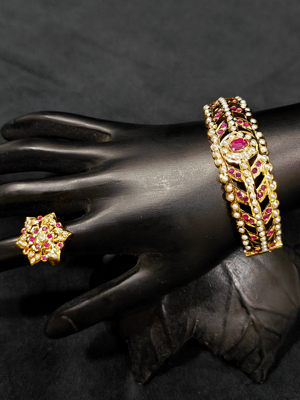 Close-up of an ornate traditional Ruby Pink and White jadau gold Bracelet with matched Ring with pearls and Colored stone. Festive outfit paired with a premium imitation Jadau bracelet with Ring in India. Close-up of a high-quality imitation Jadau bracelet with Ring for festive wear.