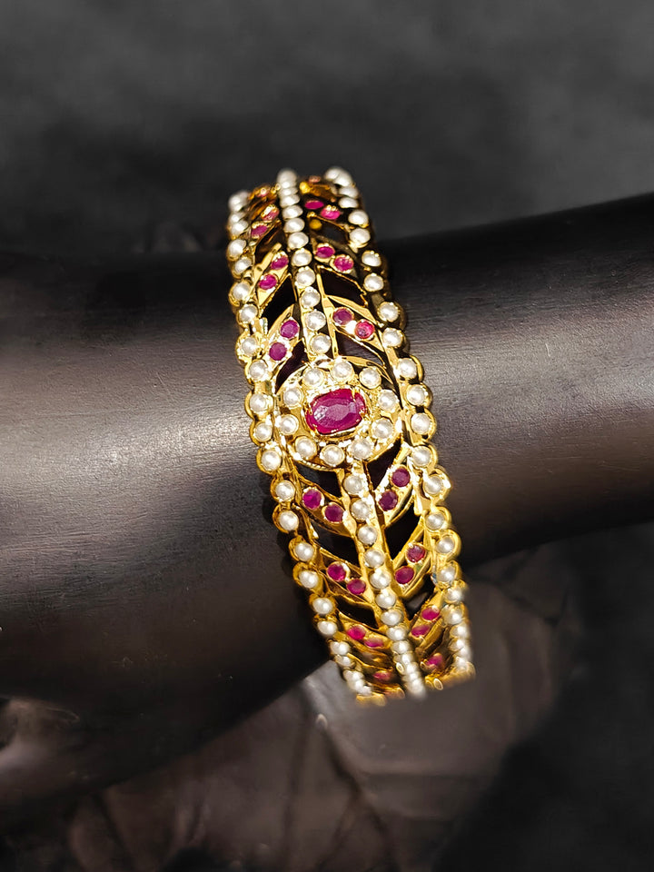 Close-up of an ornate traditional Ruby Pink and White jadau gold Bracelet with matched Ring with pearls and Colored stone. Festive outfit paired with a premium imitation Jadau bracelet with Ring in India. Close-up of a high-quality imitation Jadau bracelet with Ring for festive wear.