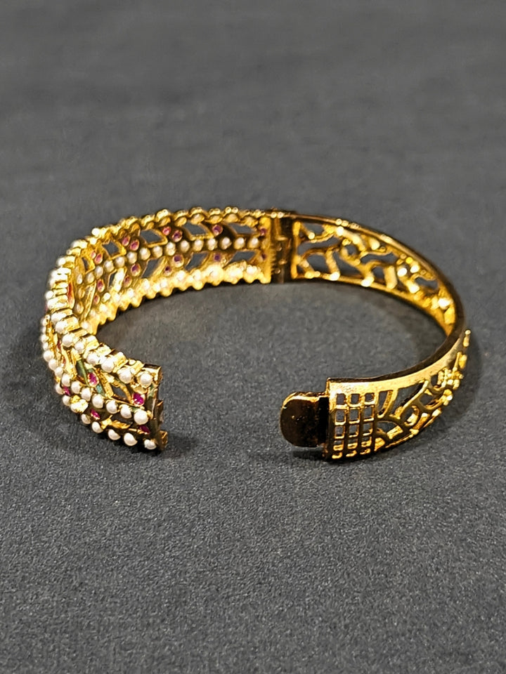 Close-up of an ornate traditional Ruby Pink and White jadau gold Bracelet with matched Ring with pearls and Colored stone. Festive outfit paired with a premium imitation Jadau bracelet with Ring in India. Close-up of a high-quality imitation Jadau bracelet with Ring for festive wear.