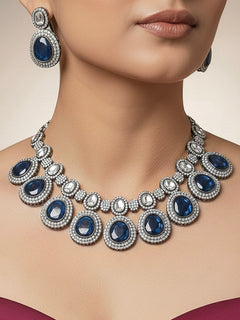 Close-up of a woman wearing an ornate Indo-western American Diamond Royal Blue Collar jewellery set and earrings with American Diamonds and Monalisa Stones. Woman styling a statement American diamond necklace with an off-shoulder gown for a reception. Close-up of a luxury American Diamond imitation necklace styled.