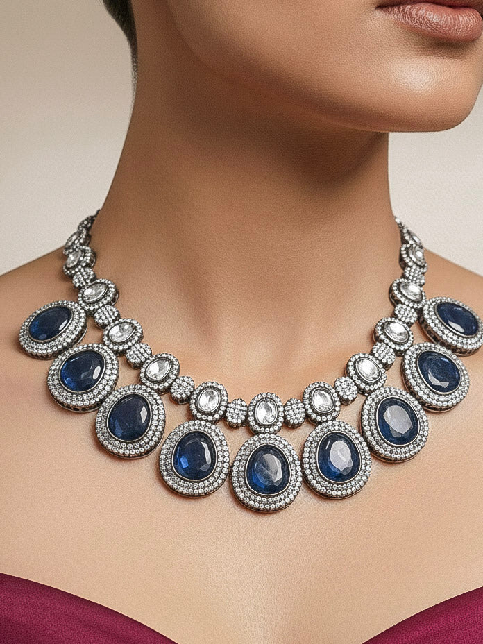 Close-up of a woman wearing an ornate Indo-western American Diamond Royal Blue Collar jewellery set and earrings with American Diamonds and Monalisa Stones. Woman styling a statement American diamond necklace with an off-shoulder gown for a reception. Close-up of a luxury American Diamond imitation necklace styled.