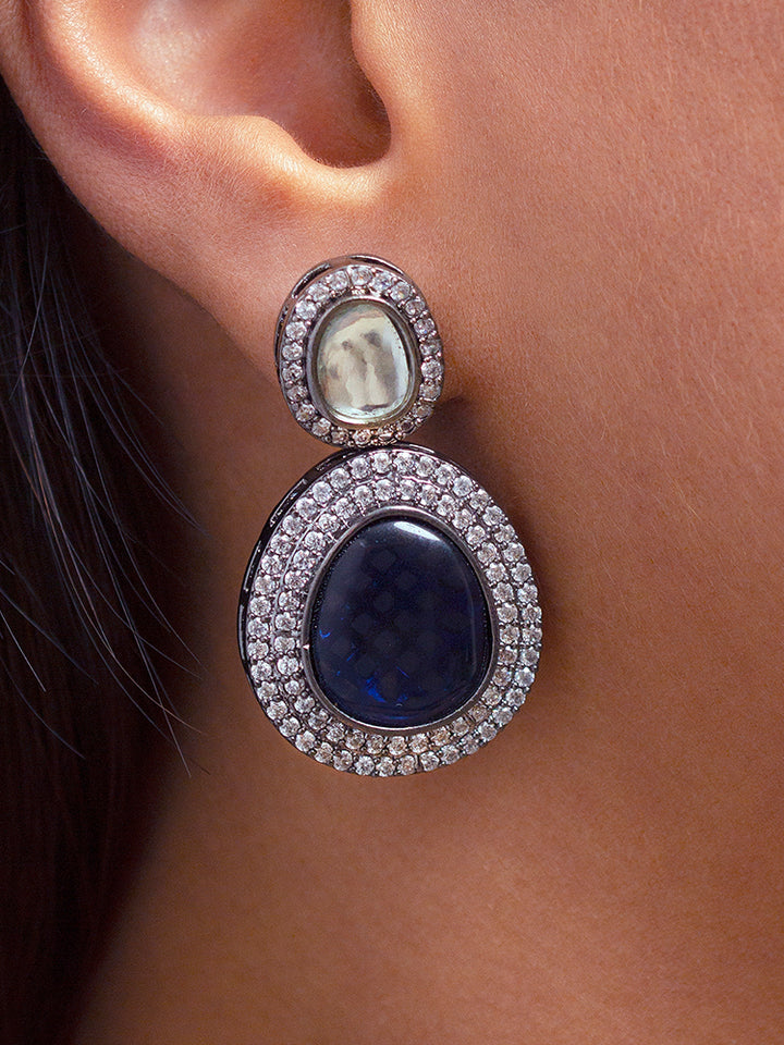 A woman with brown hair down smiles to the side, wearing the Royal Blue Elizabeth Necklace Set featuring a statement Victorian-style necklace and matching earrings with large colorful stones, paired with a sparkly dark top.
