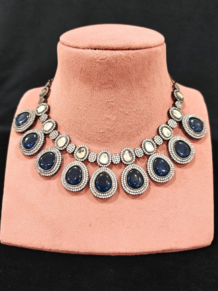 Close-up of an ornate Indo-western American Diamond Royal Blue Collar jewellery set and earrings with American Diamonds and Monalisa Stones. Woman styling a statement American diamond necklace with an off-shoulder gown for a reception. Close-up of a luxury American Diamond imitation necklace styled.
