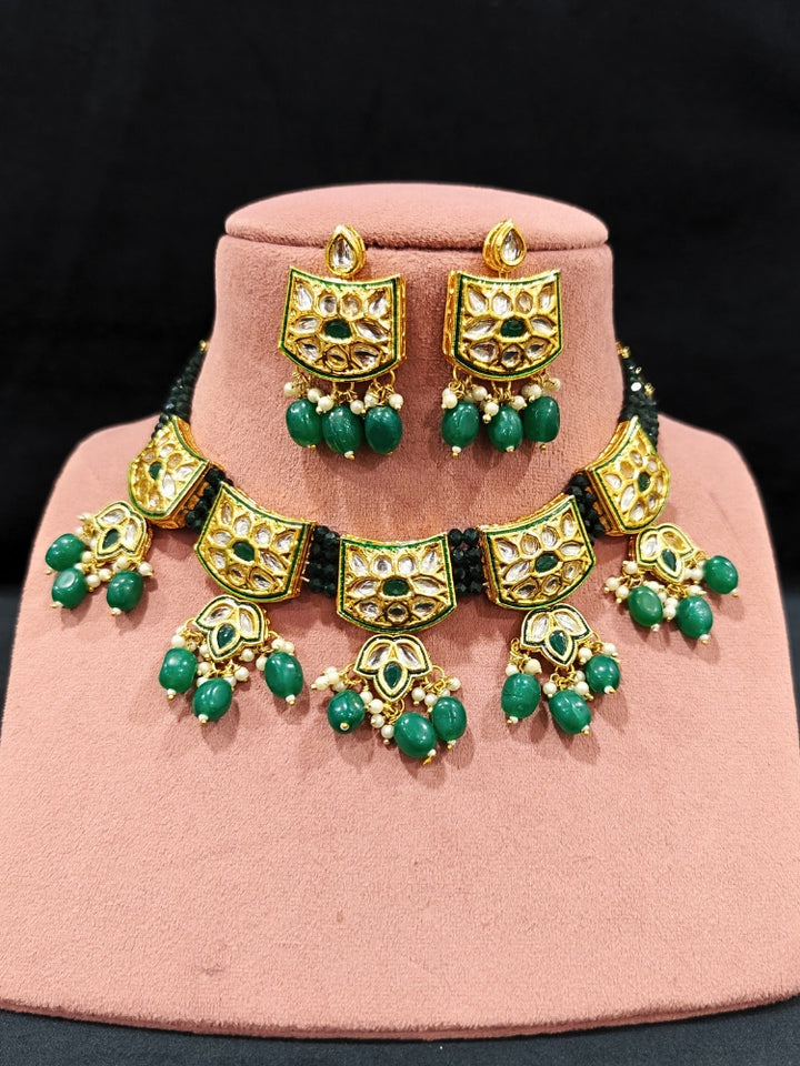 Close-up of an ornate traditional (Gold Polish) Dark Green Choker jewellery set and earrings with Pearl, Crystal stones, Kundan, Colored Stones and Tumble Beads. Mehendi ceremony look completed with a handcrafted Kundan jewelry set. Wedding celebration look enhanced with a statement Kundan necklace.