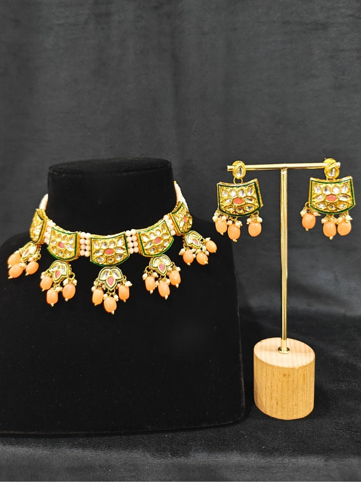 Close-up of an ornate traditional (Gold Polish) Peach Choker jewellery set and earrings with Pearl, Crystal stones, Kundan, Colored Stones and Tumble Beads. Mehendi ceremony look completed with a handcrafted Kundan jewelry set. Wedding celebration look enhanced with a statement Kundan necklace.