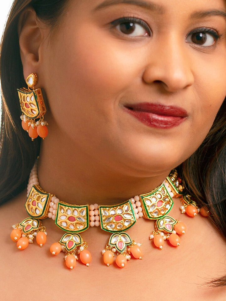 Close-up of a woman wearing an ornate traditional (Gold Polish) Peach Choker jewellery set and earrings with Pearl, Crystal stones, Kundan, Colored Stones and Tumble Beads. Mehendi ceremony look completed with a handcrafted Kundan jewelry set. Wedding celebration look enhanced with a statement Kundan necklace.
