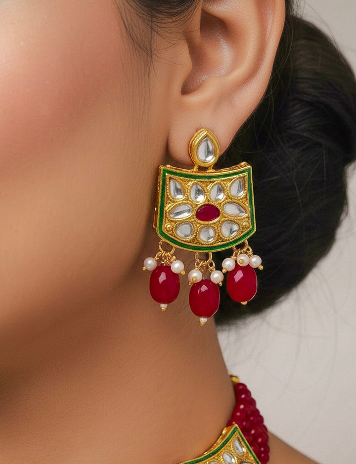 Close-up of a woman wearing an ornate traditional (Gold Polish) Red Choker jewellery set and earrings with Pearl, Crystal stones, Kundan, Colored Stones and Tumble Beads. Mehendi ceremony look completed with a handcrafted Kundan jewelry set. Wedding celebration look enhanced with a statement Kundan necklace.