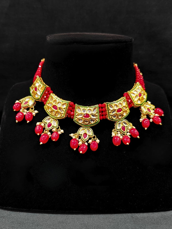 Close-up of a woman wearing an ornate traditional (Gold Polish) Red Choker jewellery set and earrings with Pearl, Crystal stones, Kundan, Colored Stones and Tumble Beads. Mehendi ceremony look completed with a handcrafted Kundan jewelry set. Wedding celebration look enhanced with a statement Kundan necklace.