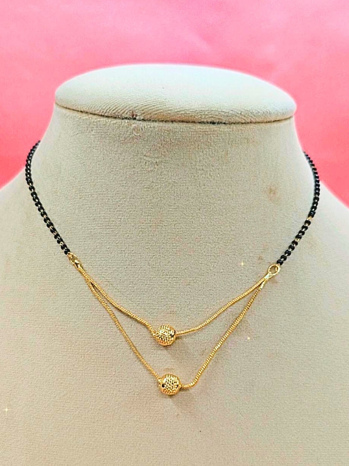 Rupali Mangalsutra—a gold necklace with black mangalsutra beads and matching earrings, pendant featuring sparkling American Diamonds—set against a cream dummy, perfect for your wedding ceremony dress. Diamond mangalsutra. Modern mangalsutra. 