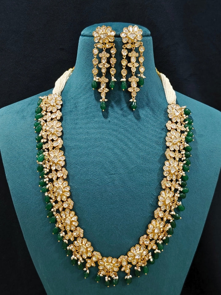 Close-up of an ornate traditional (Gold Polish) Long jewellery set and earrings with Polki, American Diamond Tumble Beads and Pearls. Wedding guest outfit styled with an elegant Polki necklace set. Woman Bridal mehendi outfit paired with a royal Polki artificial jewelry set. wearing trending Polki artificial jewelry for the wedding season in India. 