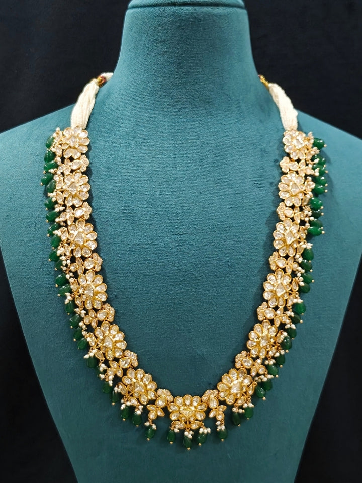 Close-up of an ornate traditional (Gold Polish) Long jewellery set and earrings with Polki, American Diamond Tumble Beads and Pearls. Wedding guest outfit styled with an elegant Polki necklace set. Woman Bridal mehendi outfit paired with a royal Polki artificial jewelry set. wearing trending Polki artificial jewelry for the wedding season in India. 
