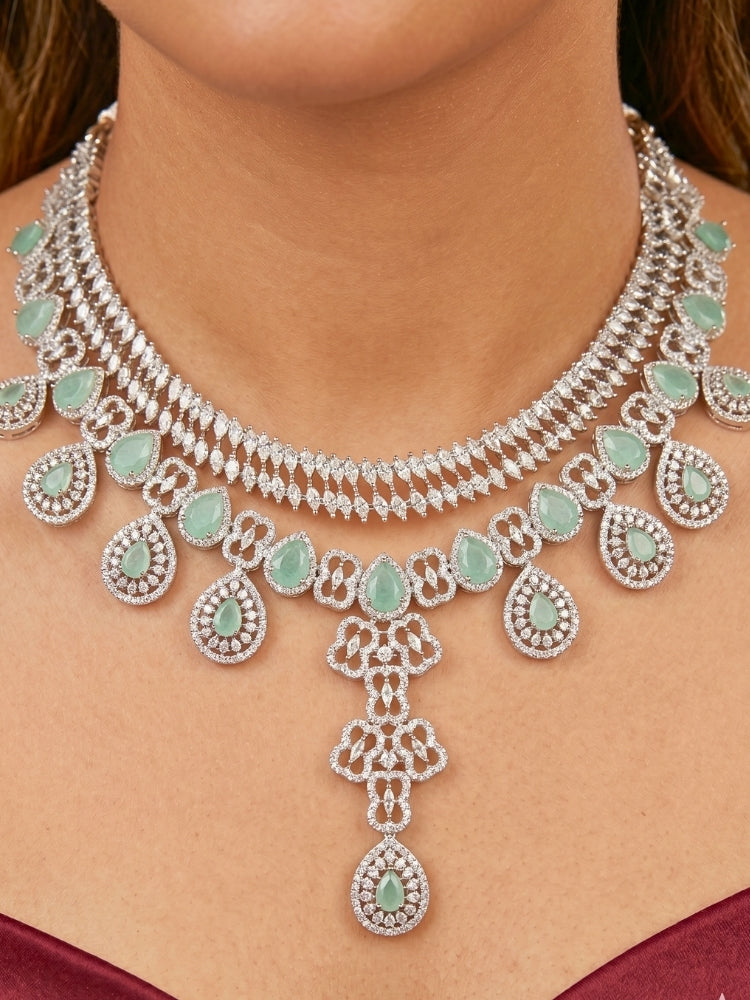 Close-up of a women wearing an ornate Western (Silver Polish) Collar Layered jewellery set and earrings with American Diamond and Mint Green Colored Stones. Reception-ready look featuring a statement American diamond jewelry set. Elegant wedding jewelry look featuring a premium artificial American diamond necklace. 