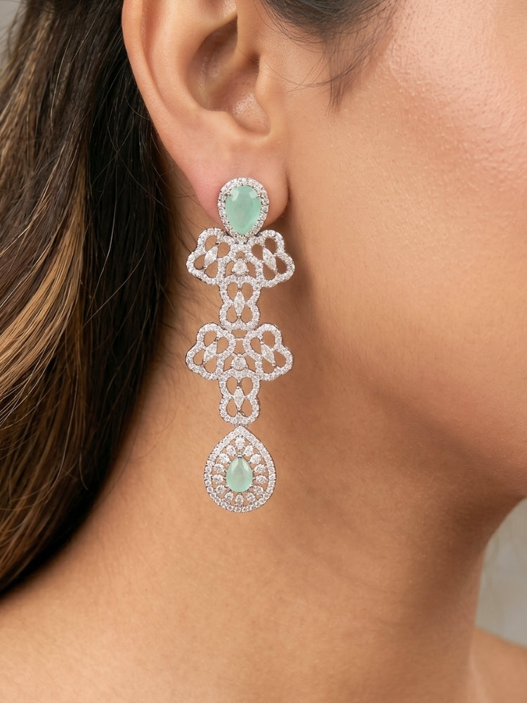 Close-up of a women wearing an ornate Western (Silver Polish) Collar Layered jewellery set and earrings with American Diamond and Mint Green Colored Stones. Reception-ready look featuring a statement American diamond jewelry set. Elegant wedding jewelry look featuring a premium artificial American diamond necklace. 