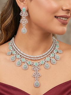 Close-up of a women wearing an ornate Western (Silver Polish) Collar Layered jewellery set and earrings with American Diamond and Mint Green Colored Stones. Reception-ready look featuring a statement American diamond jewelry set. Elegant wedding jewelry look featuring a premium artificial American diamond necklace. 