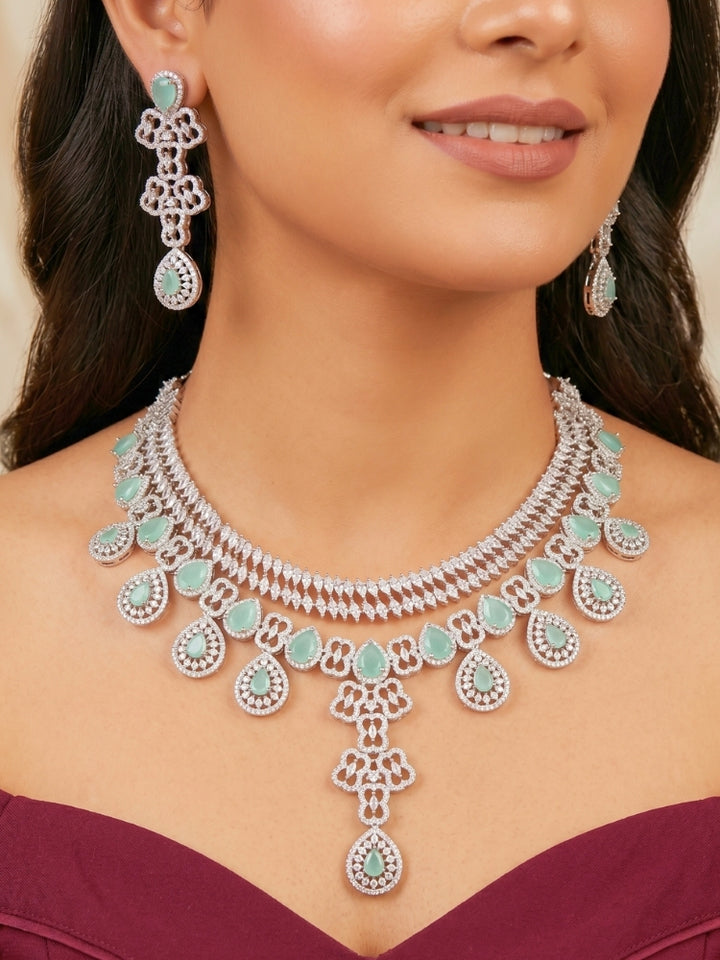 Close-up of a women wearing an ornate Western (Silver Polish) Collar Layered jewellery set and earrings with American Diamond and Mint Green Colored Stones. Reception-ready look featuring a statement American diamond jewelry set. Elegant wedding jewelry look featuring a premium artificial American diamond necklace. 