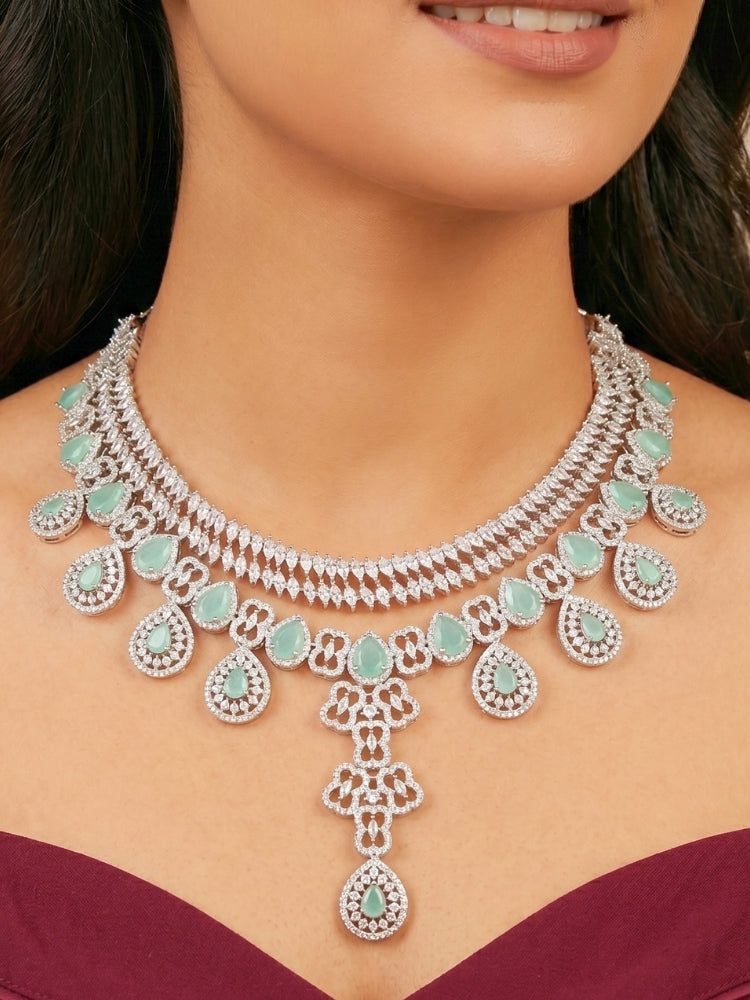 Close-up of a women wearing an ornate Western (Silver Polish) Collar Layered jewellery set and earrings with American Diamond and Mint Green Colored Stones. Reception-ready look featuring a statement American diamond jewelry set. Elegant wedding jewelry look featuring a premium artificial American diamond necklace. 