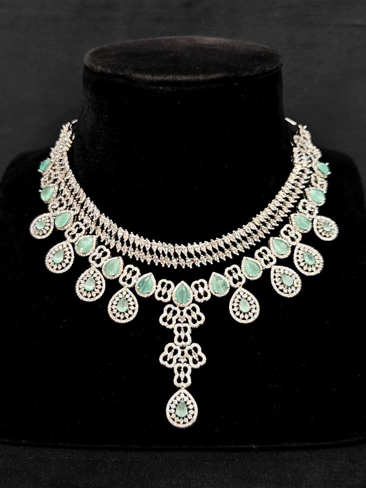 Close-up of an ornate Western (Silver Polish) Collar Layered jewellery set and earrings with American Diamond and Mint Green Colored Stones. Reception-ready look featuring a statement American diamond jewelry set. Elegant wedding jewelry look featuring a premium artificial American diamond necklace.