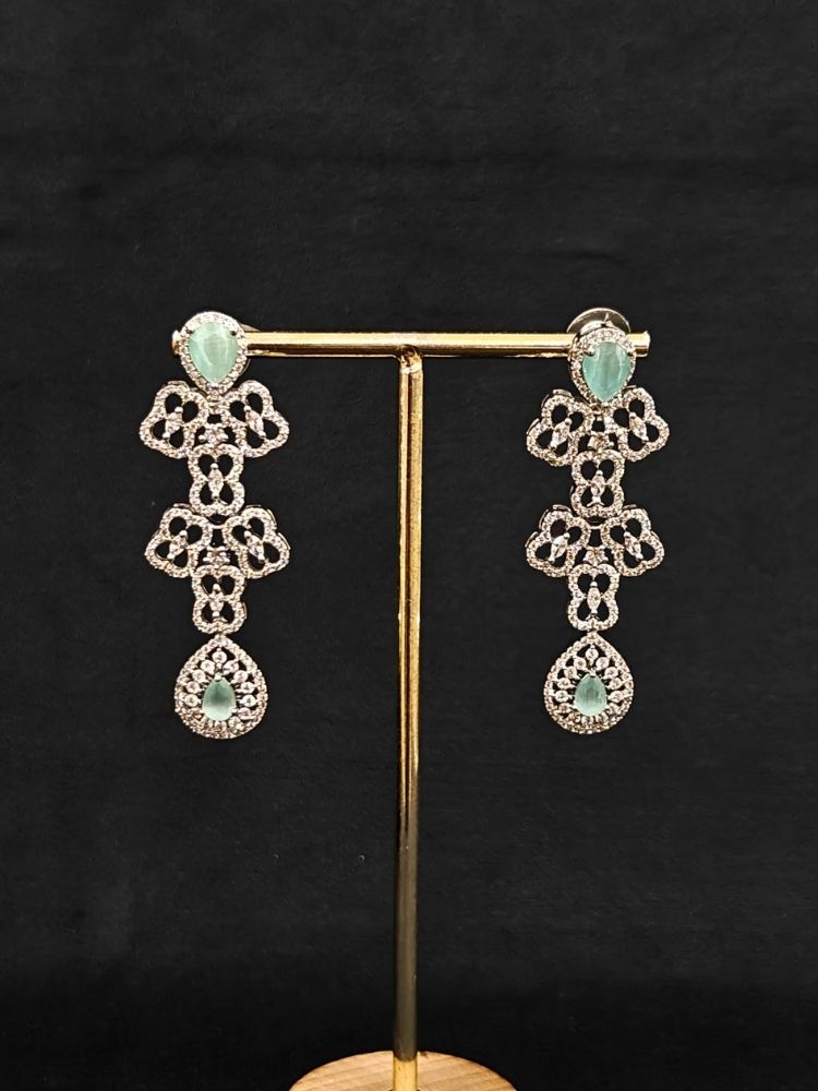 Close-up of an ornate Western (Silver Polish) Collar Layered jewellery set and earrings with American Diamond and Mint Green Colored Stones. Reception-ready look featuring a statement American diamond jewelry set. Elegant wedding jewelry look featuring a premium artificial American diamond necklace.