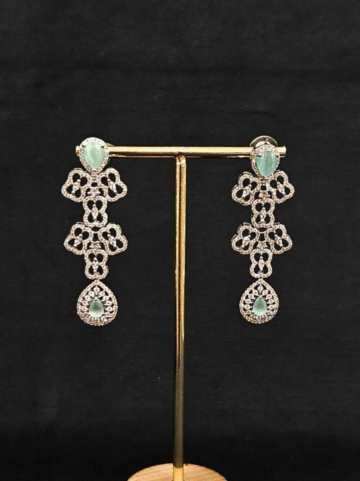 Close-up of an ornate Western (Silver Polish) Collar Layered jewellery set and earrings with American Diamond and Mint Green Colored Stones. Reception-ready look featuring a statement American diamond jewelry set. Elegant wedding jewelry look featuring a premium artificial American diamond necklace.