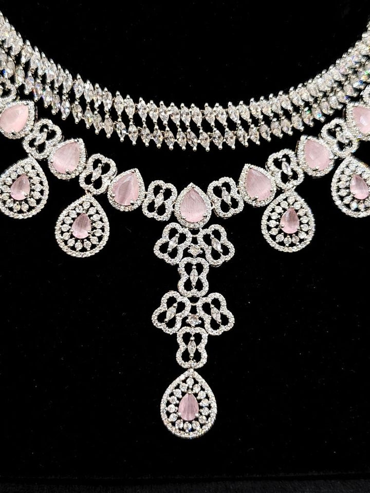 Close-up of an ornate Western (Silver Polish) Collar Layered jewellery set and earrings with American Diamond and Mint Pink Colored Stones. Reception-ready look featuring a statement American diamond jewelry set. Elegant wedding jewelry look featuring a premium artificial American diamond necklace.