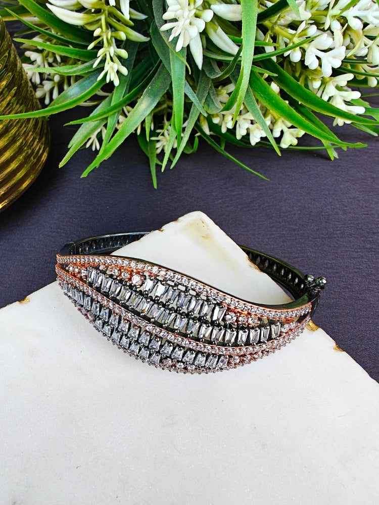 The Samantha Bracelet, an openable bracelet adorned with rows of sparkling clear American Diamonds and rose gold stones, is displayed on a white marble slab with green leafy plants in the background.