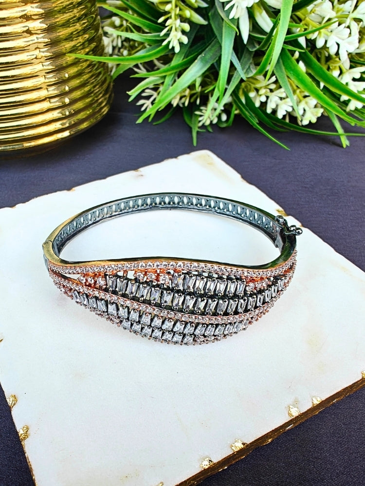 The Samantha Bracelet, an openable bracelet adorned with rows of sparkling clear American Diamonds and rose gold stones, is displayed on a white marble slab with green leafy plants in the background.