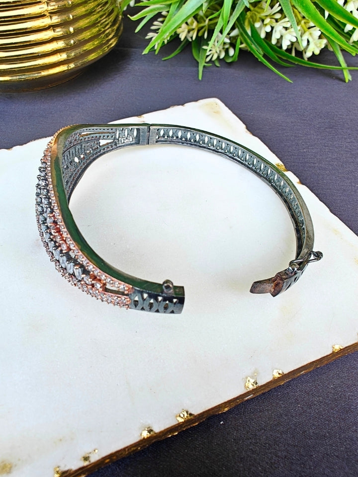 The Samantha Bracelet, an openable bracelet adorned with rows of sparkling clear American Diamonds and rose gold stones, is displayed on a white marble slab with green leafy plants in the background.