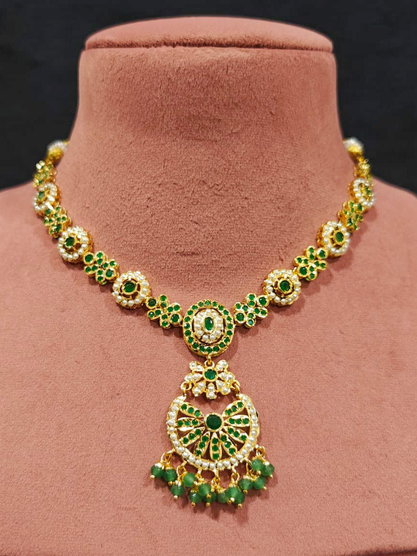 Close-up of an ornate traditional collar Green jadau gold jewellery set and jadau earrings with pearls and Green gemstones. Mehendi function outfit styled with a lightweight Jadau necklace. Close-up of high-quality Jadau artificial necklace craftsmanship.