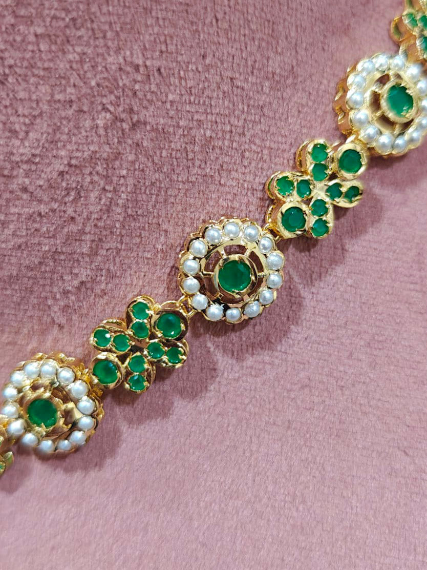 Close-up of an ornate traditional collar Green jadau gold jewellery set and jadau earrings with pearls and Green gemstones. Mehendi function outfit styled with a lightweight Jadau necklace. Close-up of high-quality Jadau artificial necklace craftsmanship.