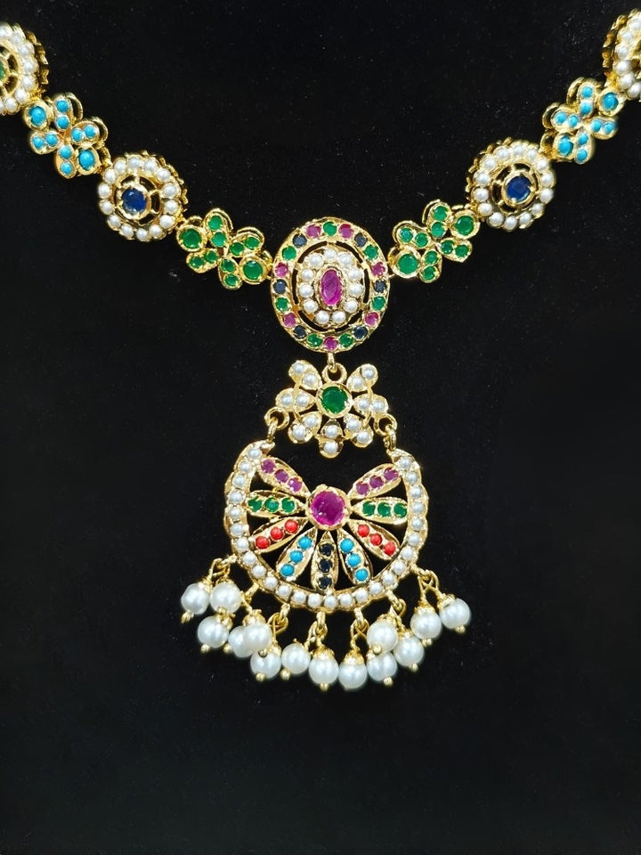 Close-up of an ornate traditional collar Navratan jadau gold jewellery set and jadau earrings with pearls and Navratan gemstones. A royal Jadau necklace for festive events in India. Styling inspiration with a premium Jadau imitation necklace.