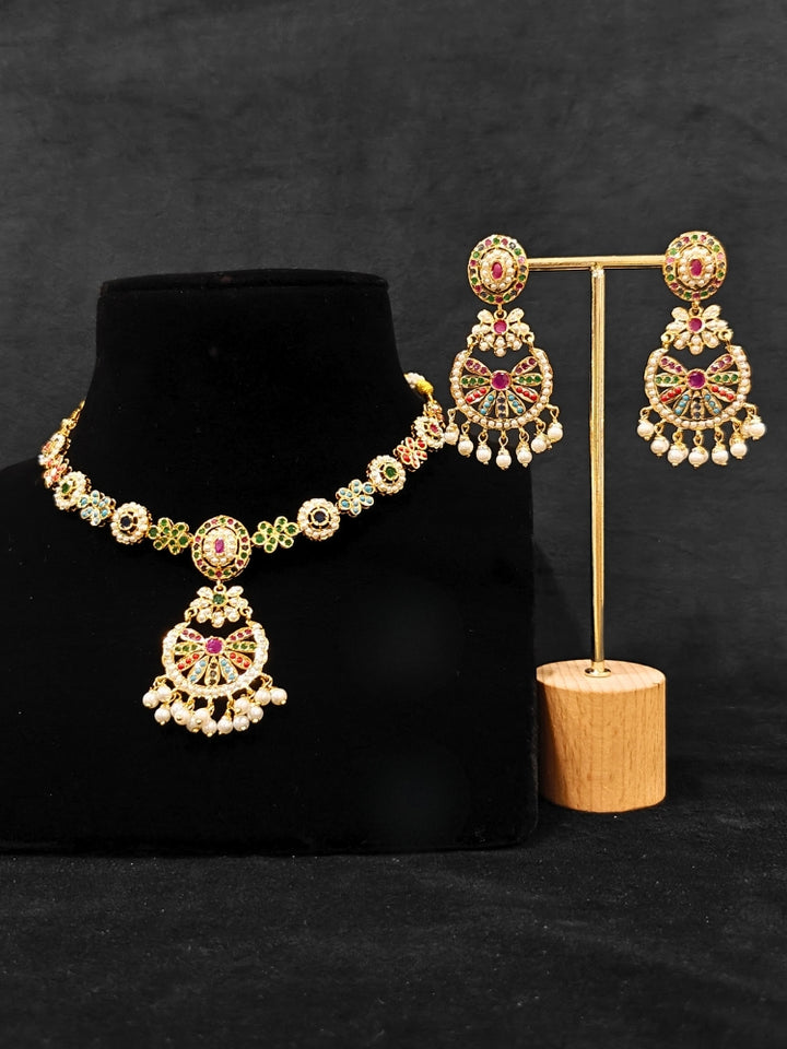 Close-up of an ornate traditional collar Navratan jadau gold jewellery set and jadau earrings with pearls and Navratan gemstones. A royal Jadau necklace for festive events in India. Styling inspiration with a premium Jadau imitation necklace.