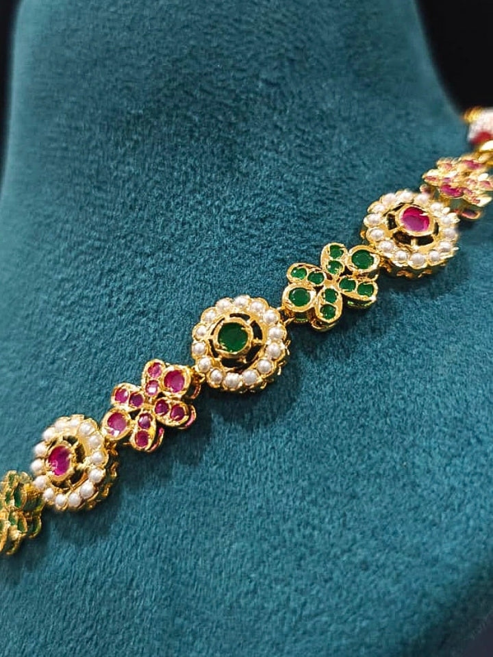 Close-up of an ornate traditional Collar Ruby Pink & Green jadau gold jewellery set and jadau earrings with pearls and Color Stone. Elegant  look featuring a luxury Jadau artificial jewelry set. Close-up of high-quality Jadau artificial necklace craftsmanship.