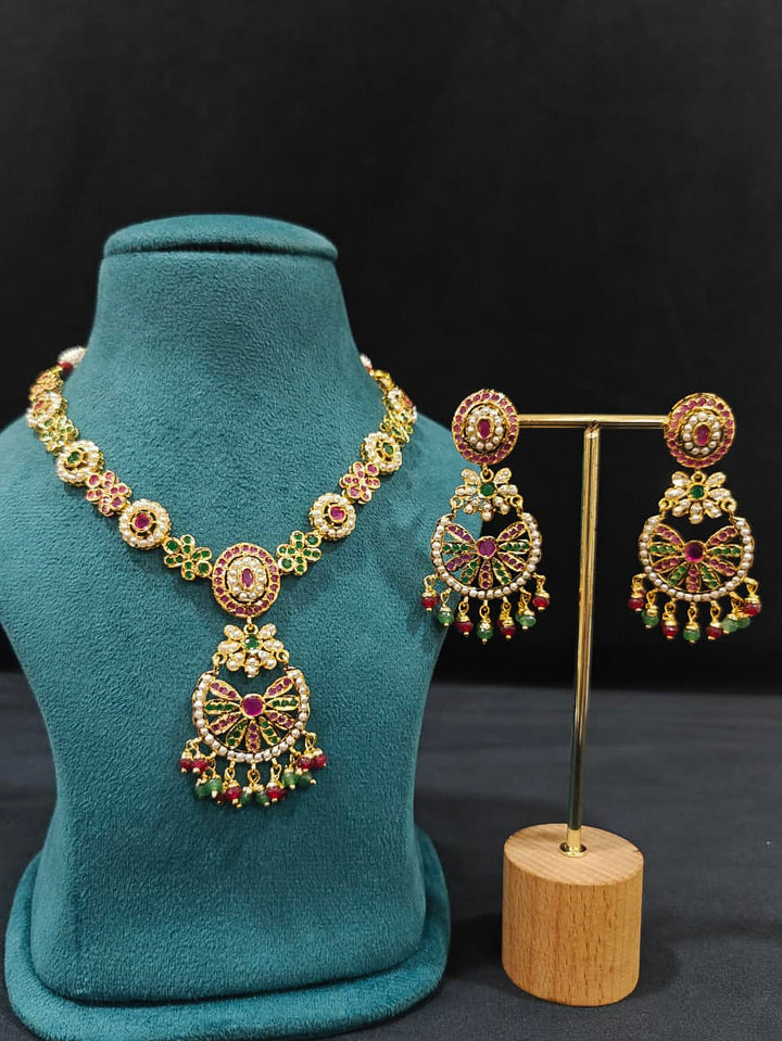 Close-up of an ornate traditional Collar Ruby Pink & Green jadau gold jewellery set and jadau earrings with pearls and Color Stone. Elegant  look featuring a luxury Jadau artificial jewelry set. Close-up of high-quality Jadau artificial necklace craftsmanship.