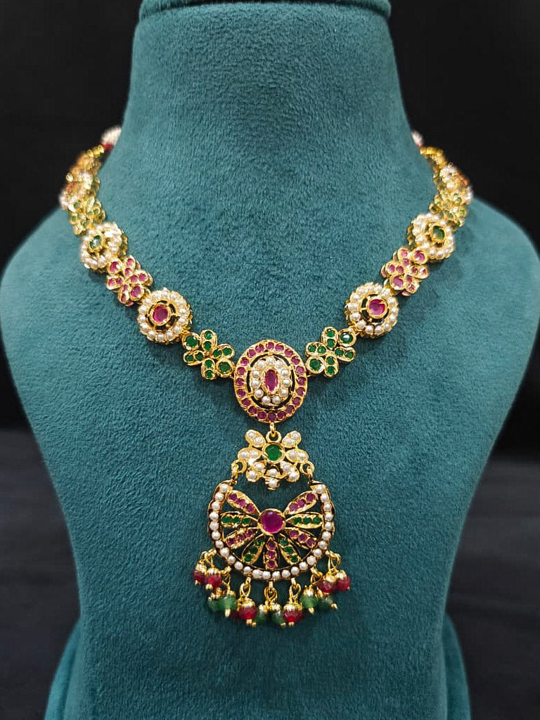 Close-up of an ornate traditional Collar Ruby Pink & Green jadau gold jewellery set and jadau earrings with pearls and Color Stone. Elegant  look featuring a luxury Jadau artificial jewelry set. Close-up of high-quality Jadau artificial necklace craftsmanship.