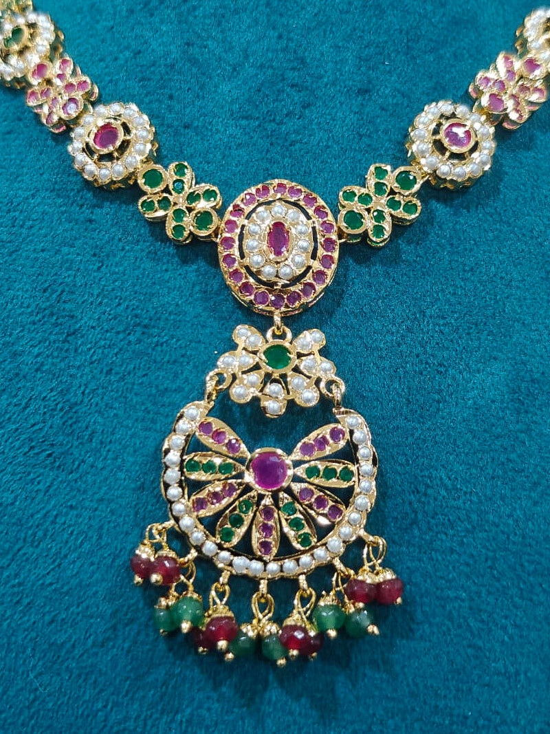 Close-up of an ornate traditional Collar Ruby Pink & Green jadau gold jewellery set and jadau earrings with pearls and Color Stone. Elegant  look featuring a luxury Jadau artificial jewelry set. Close-up of high-quality Jadau artificial necklace craftsmanship.