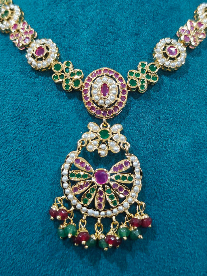 Close-up of an ornate traditional Collar Ruby Pink & Green jadau gold jewellery set and jadau earrings with pearls and Color Stone. Elegant  look featuring a luxury Jadau artificial jewelry set. Close-up of high-quality Jadau artificial necklace craftsmanship.