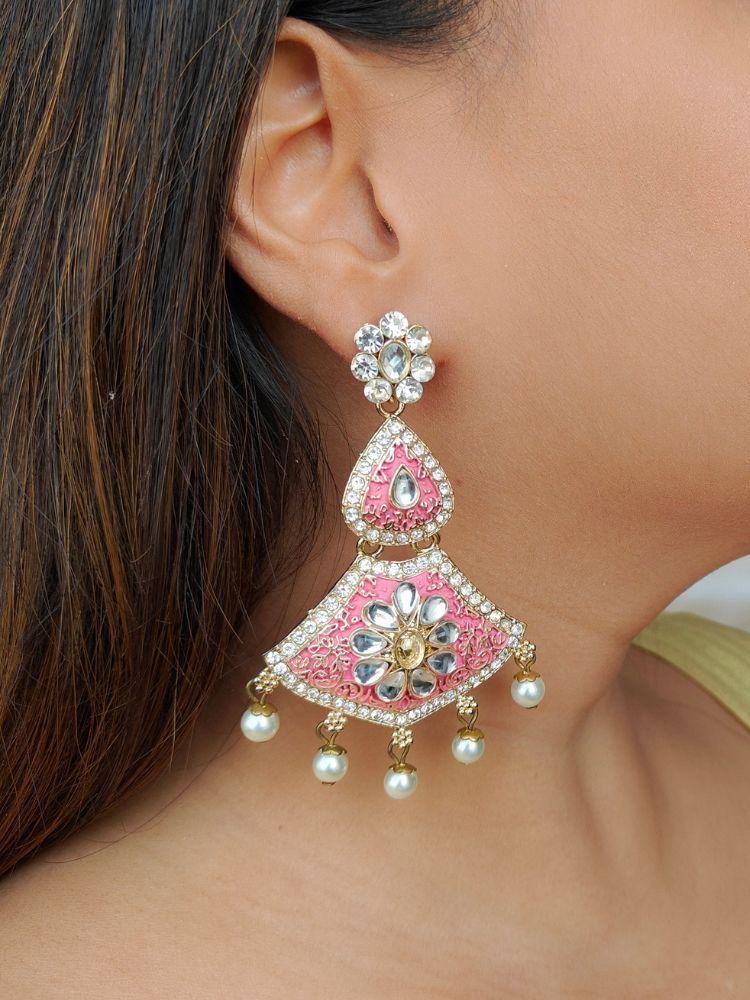 A close-up of a womans ear adorned with Sanjana Pink Earrings, featuring turquoise enamel, gold accents, american diamonds, and pearl beads—ideal for elevating a wedding ceremony look. She has straight brown hair and light brown skin.
