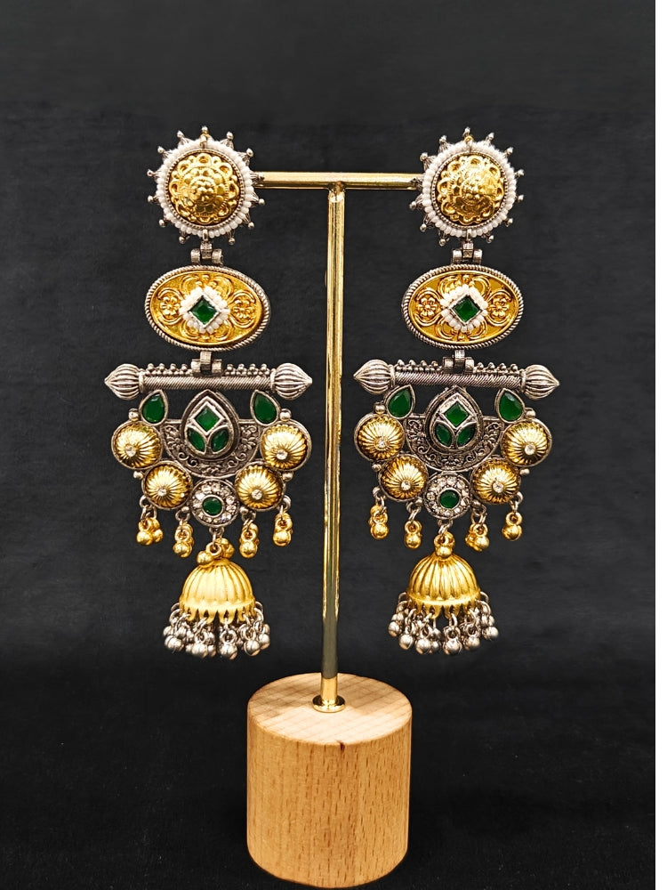 A close-up of a Sanjukta Green Earrings, featuring ornate multicolored designs, American Diamond accents, gold and maroon details, intricate patterns, dangling beads, and a bell-shaped charm at the bottom. These are oxidized german silver earrings perfect for navratri earrings. 