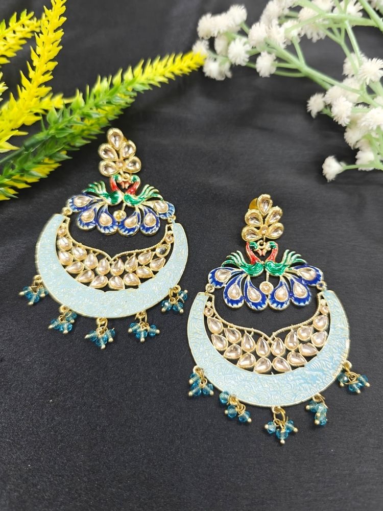 Sarika Blue Earrings, featuring large, ornate peacock designs with gold, blue, green, and red detailing, embellished with Kundan and pearls and finished with small dangling red beads, shown on a black background. 
