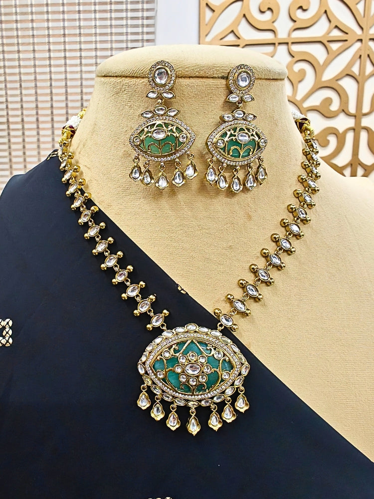 A mannequin showcases the Anuradha Sea Green Necklace Set—an ornate gold Kundan jewelry necklace with matching earrings, embellished with red and white enamel, floral motifs, and teardrop crystals.