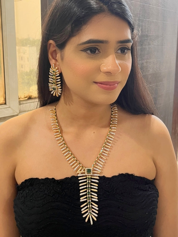A woman in a strapless black dress showcases the Selvaggia long Necklace Set, featuring sparkling American Diamonds and white stones, with large earrings and an intricate green necklace adorned with gemstone accents.