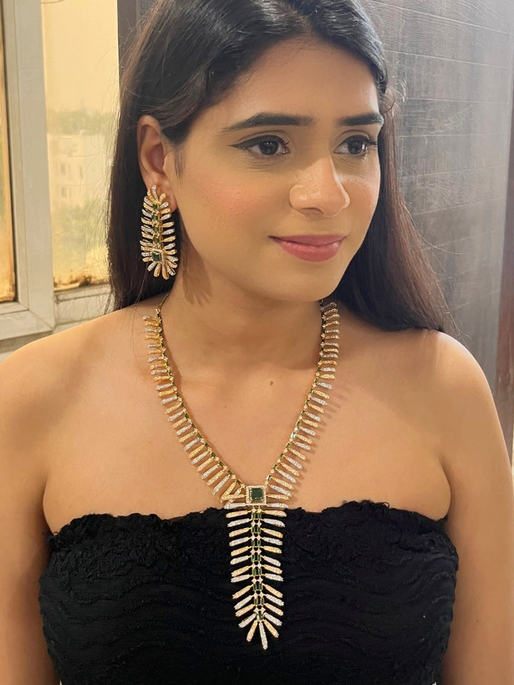 A woman in a strapless black dress showcases the Selvaggia long Necklace Set, featuring sparkling American Diamonds and white stones, with large earrings and an intricate green necklace adorned with gemstone accents.
