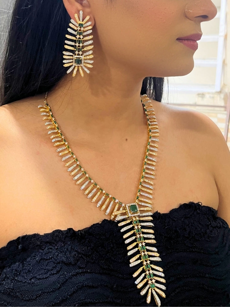 A woman in a strapless black dress showcases the Selvaggia long Necklace Set, featuring sparkling American Diamonds and white stones, with large earrings and an intricate green necklace adorned with gemstone accents.