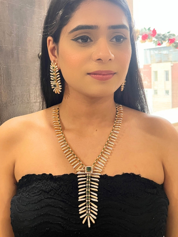A woman in a strapless black dress showcases the Selvaggia long Necklace Set, featuring sparkling American Diamonds and white stones, with large earrings and an intricate green necklace adorned with gemstone accents.