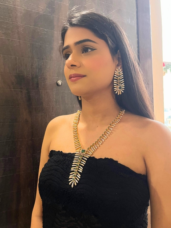 A woman in a strapless black dress showcases the Selvaggia long Necklace Set, featuring sparkling American Diamonds and white stones, with large earrings and an intricate green necklace adorned with gemstone accents.